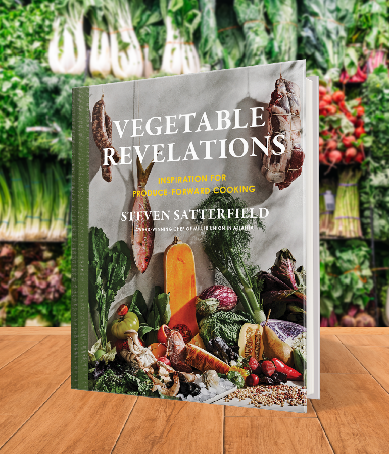 cookbook that says vegetable revelations with a variety of vegetables; on wooden table with vegetables and plants behind it