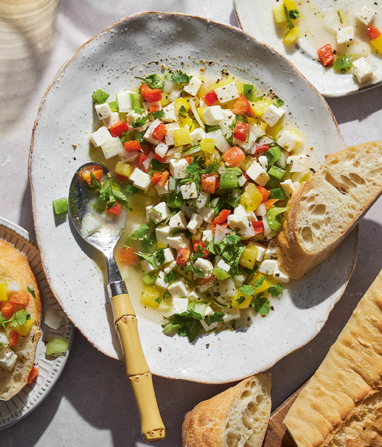 plate with spoon, bread and queso fresco which includes cheese cut into small cubes, red, yellow and green peppers, onion and cilantro