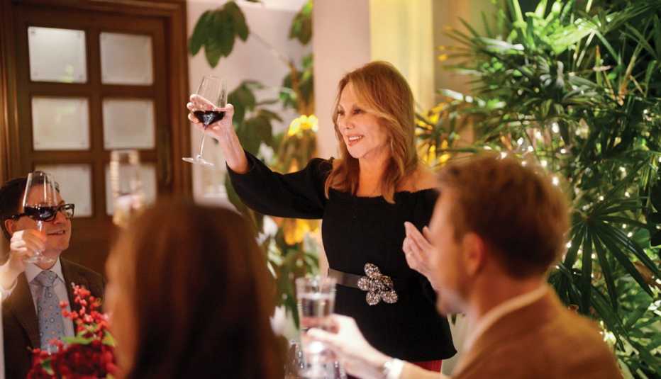 marlo thomas standing, raising glass of wine, facing people sitting at table