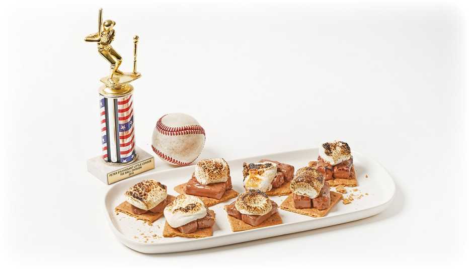 seven milky way melt smores on a white plate next to a baseball and baseball trophy