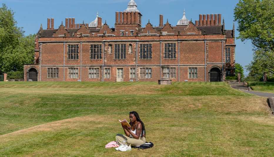 person sitting on grass, reading book outside of big building