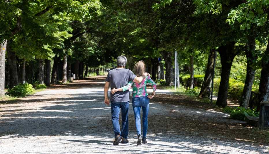 back view of max weinberg and wife becky walking on pavement with arm around each other; trees on both sides