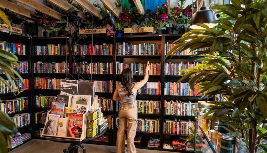 Bookcase with many books on it; woman grabbing book in section under a sign that says mystery and suspense