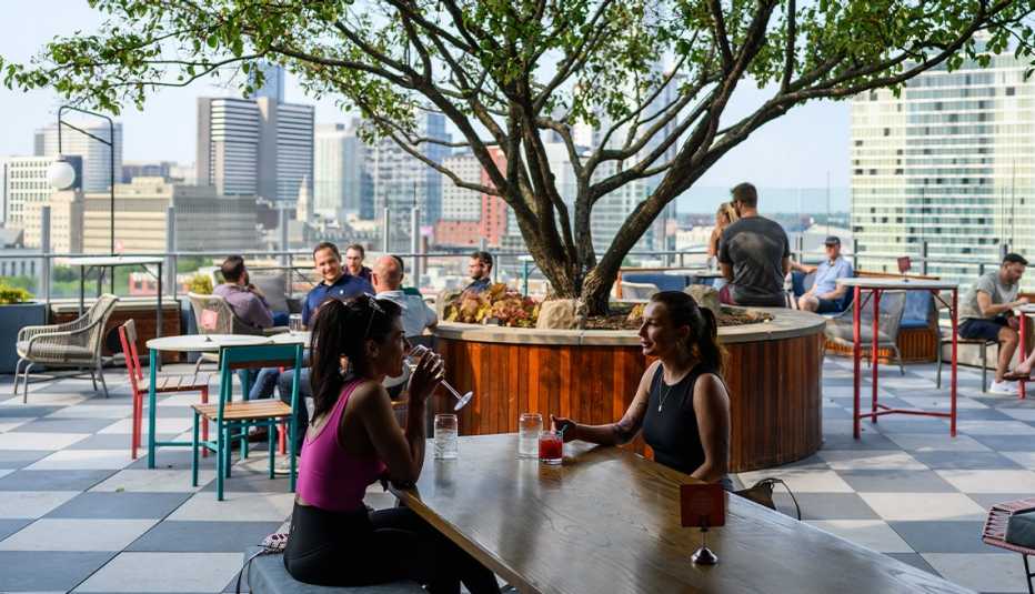 people sitting at tables, drinking at rooftop bar overlooking city