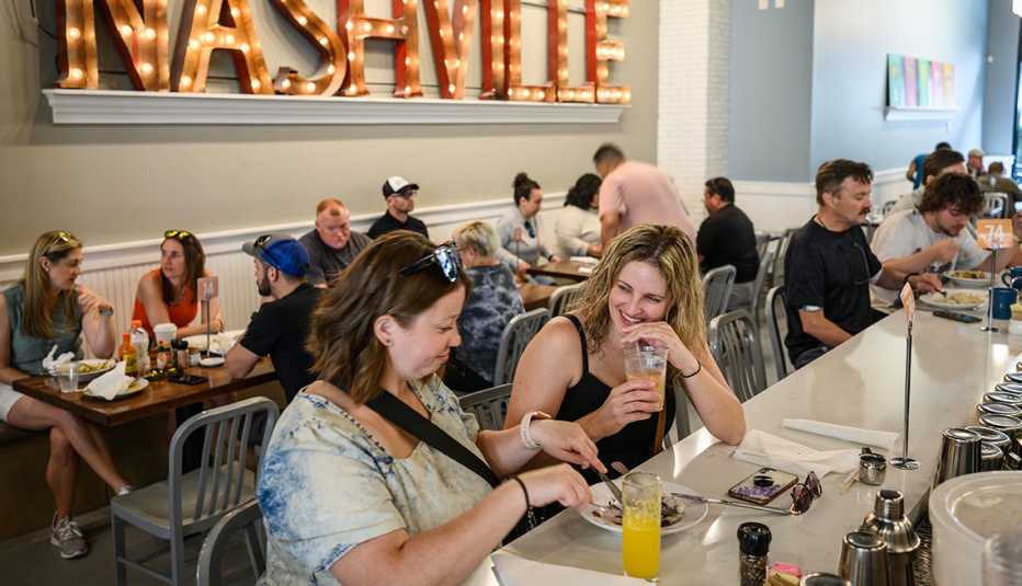 people eating and drinking at tables in restaurant; light up nashville sign on the wall