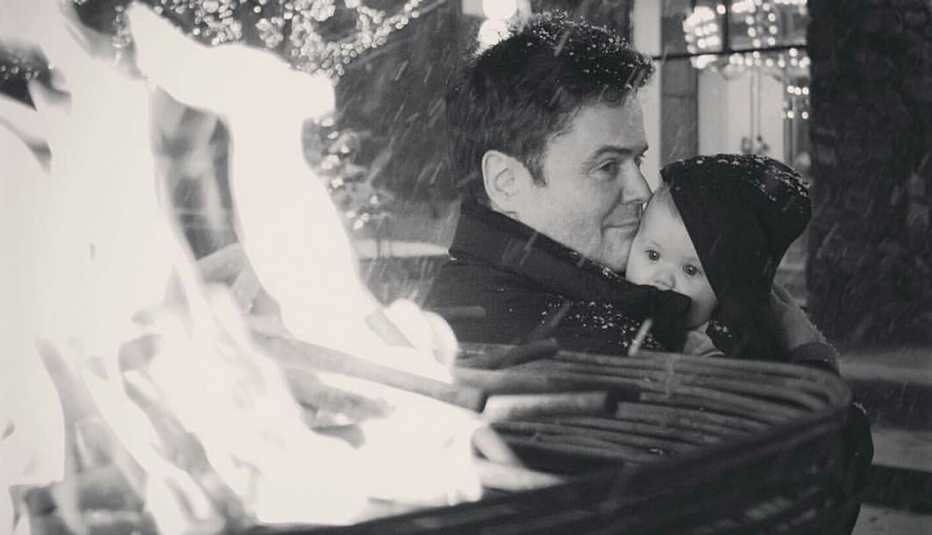 donny osmond holding baby outside next to fire while snow falls