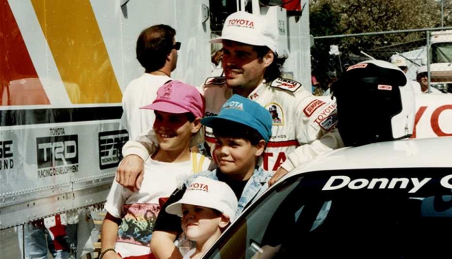 donny osmond wearing toyota racing outfit standing next to his car with three kids in front of him