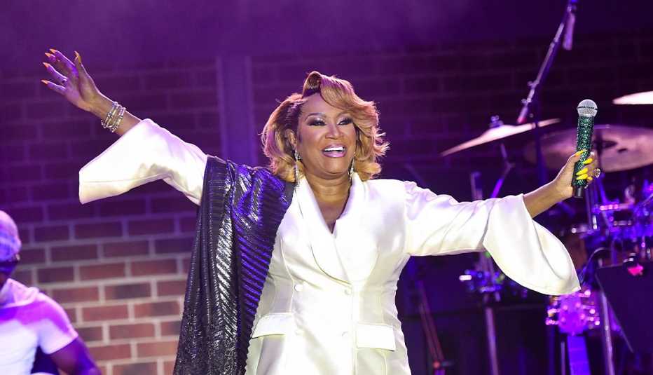 patti labelle on stage holding microphone in left hand; right arm straight out to side; drum set behind her on right side of photo