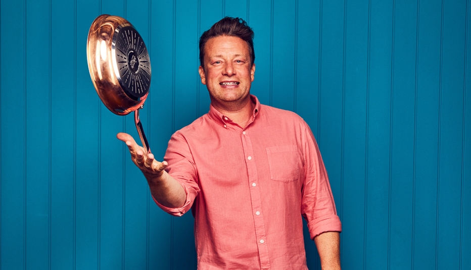jamie oliver balancing a pan on his right hand, standing in front of blue wall with vertical stripes