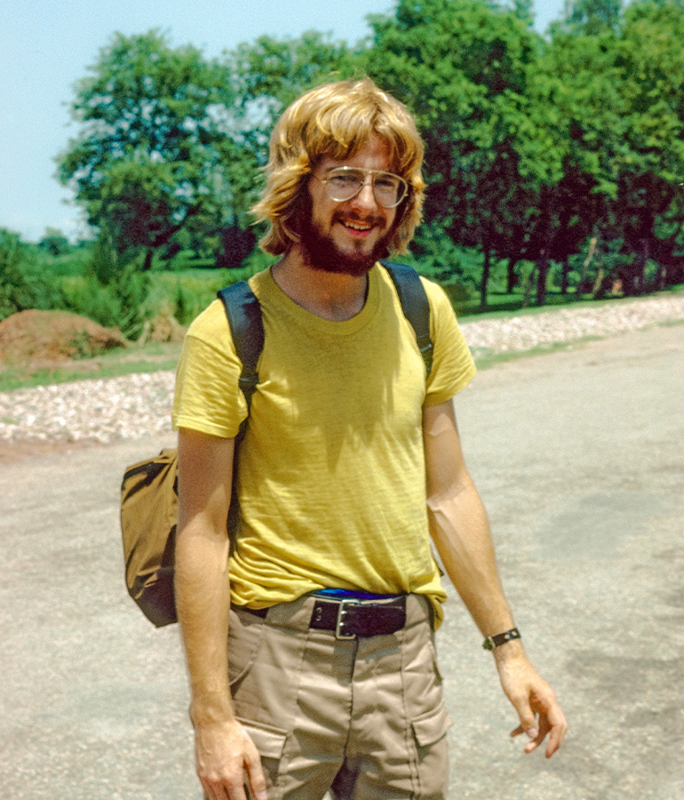 young rick steves wearing backpack outdoors with trees behind him