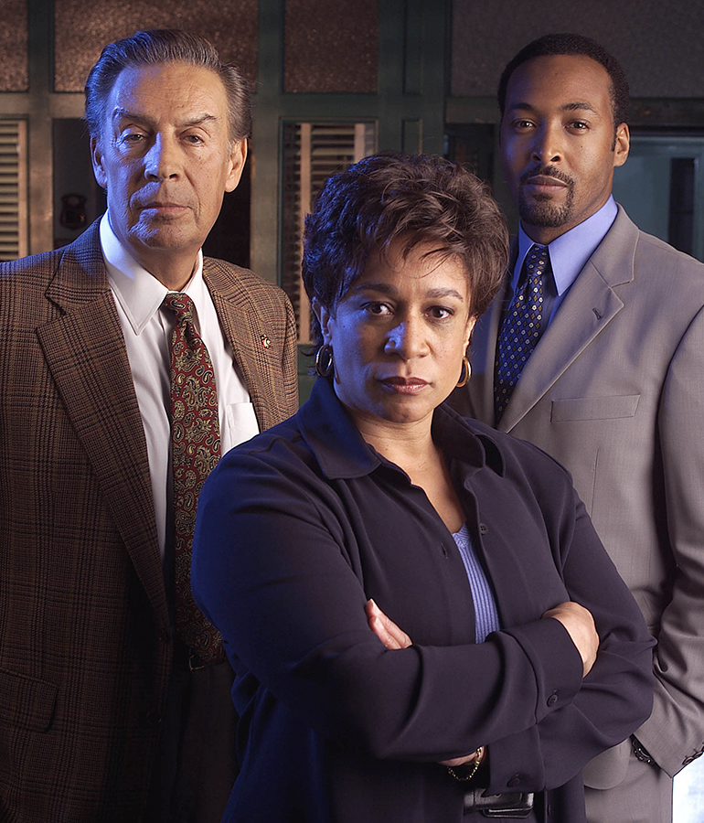 S. Epatha Merkerson with arms crossed standing in front of Jerry Orbach and Jesse L. Martin in Law and Order