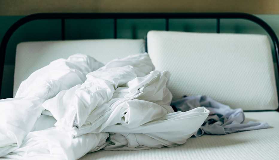 bedsheets crumbled up on top of bed; two pillows without pillowcases on bed