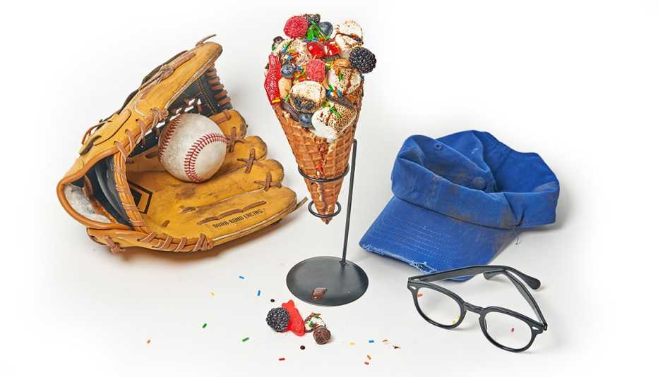 smore parfait in a waffle cone overflowing with berries, toasted marshmallows and candy, and a baseball in a glove, a blue baseball hat and a pair of 1960s-style eyeglasses