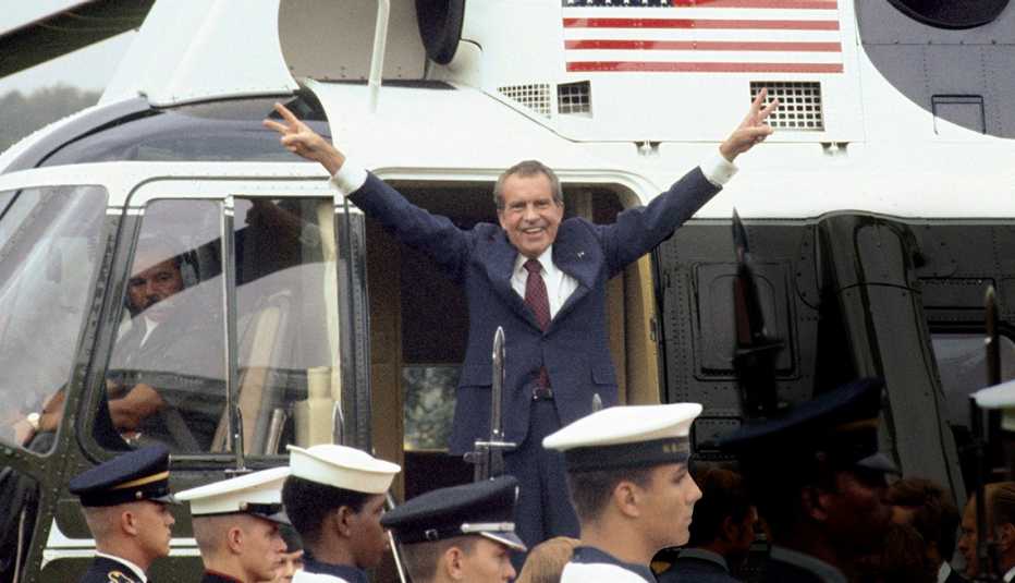 Richard Nixon standing in helicopter doorway, raising both arms in the air in V formation, giving peace signs