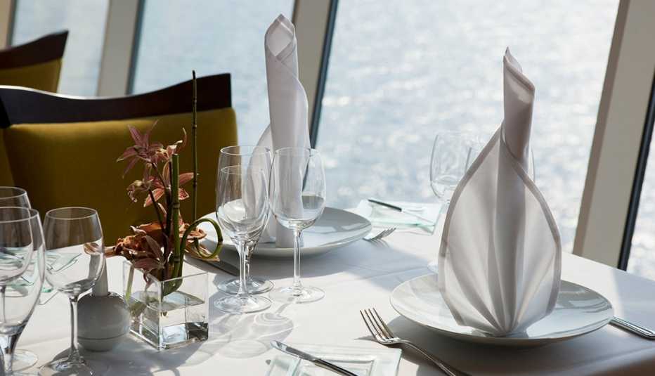 table set with plates, glasses, napkins and silverware next to window overlooking a body of water