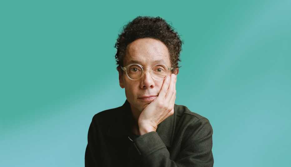 malcolm gladwell with face resting on hand against teal ombre background