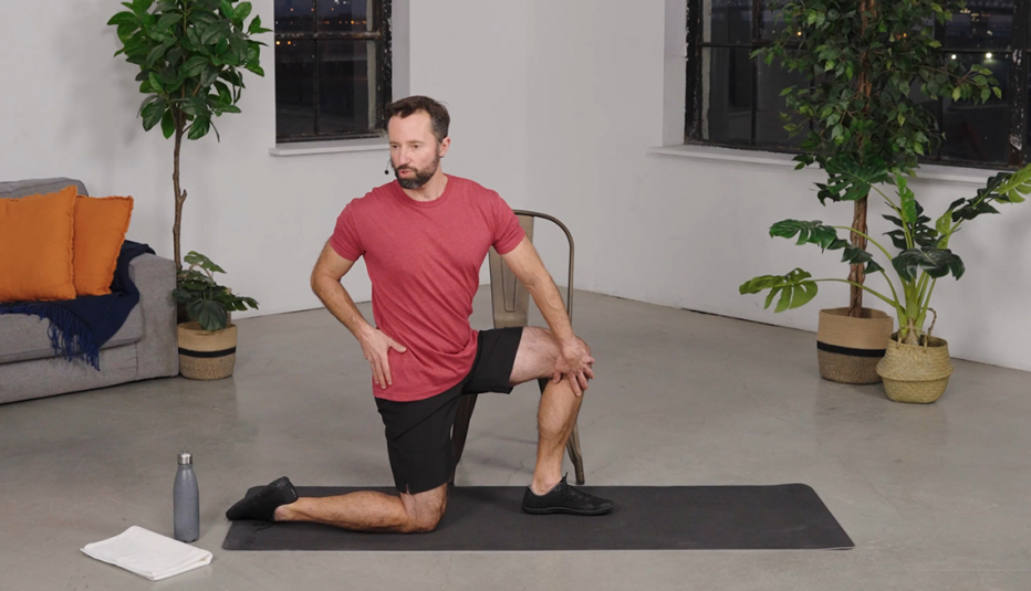 Farrell Kaufman doing a twist on one knee on a mat in a room with plants