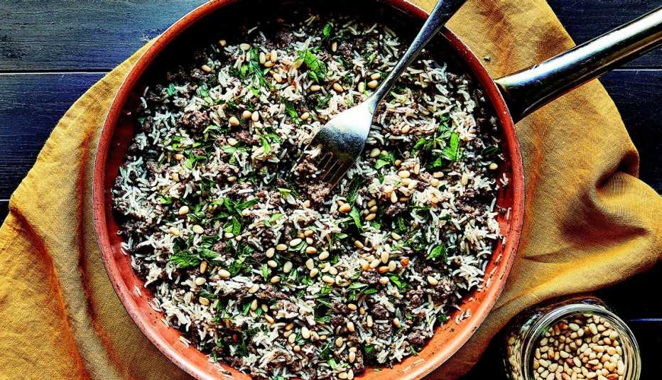 rice with ground beef, pine nuts and spices in pan with fork in it