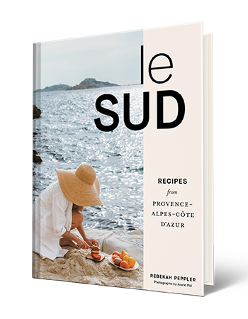 Book cover that says Le Sud: Recipes from Provence-Alpes-Côte d’Azur, Rebekah Peppler; Woman cutting food next to body of water on cover