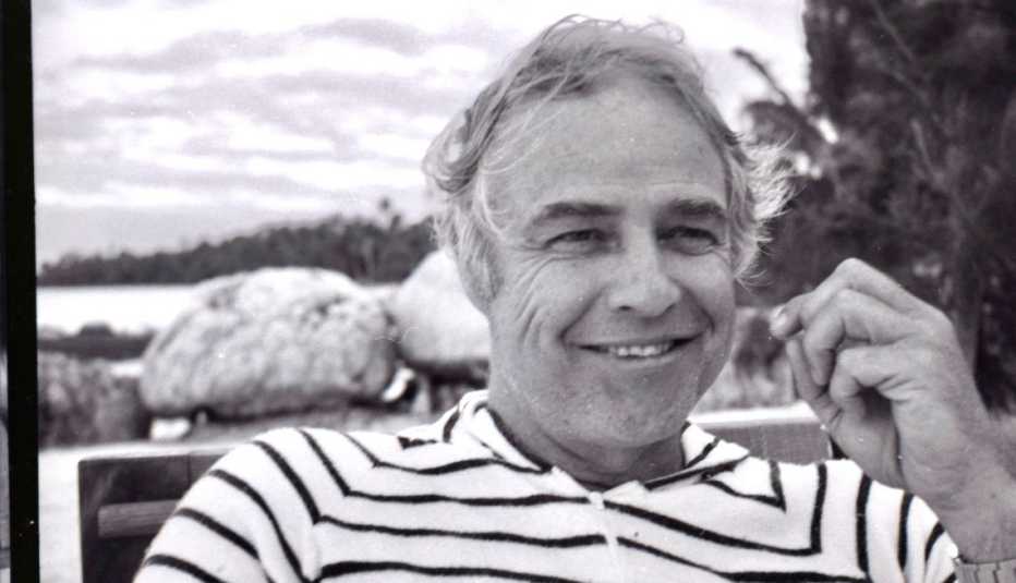 black and white image of Marlon Brando smiling with a view of water and island behind him
