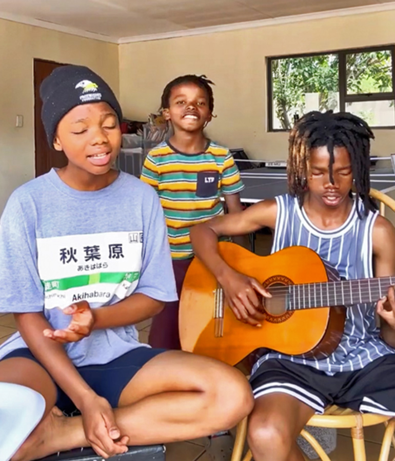 the three members of Biko's Manna in a room, one of them playing guitar and one singing