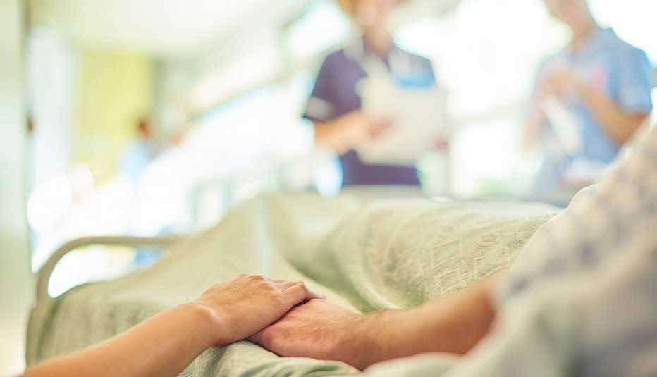 close up of a woman holding the hand of her dad who is in a hospital bed