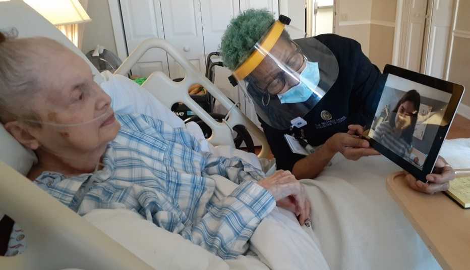 a nursing home assistant wearing p p e holds a tablet up for a woman to see in her bed
