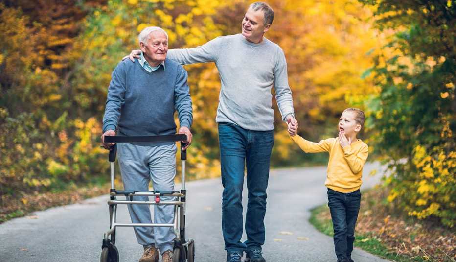Man using a walker walks through a park with his adult son and young grandson