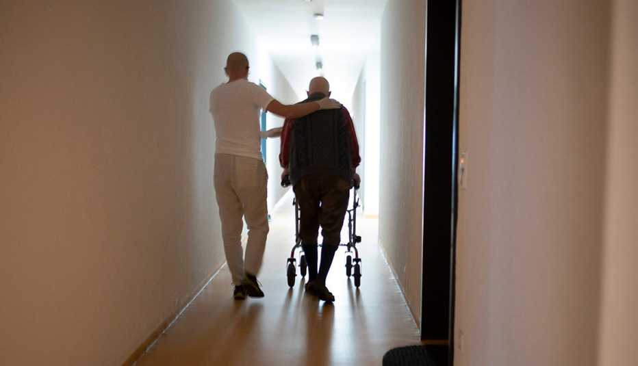 A male nurse helping a man using a walker walk down a nursing home hallway