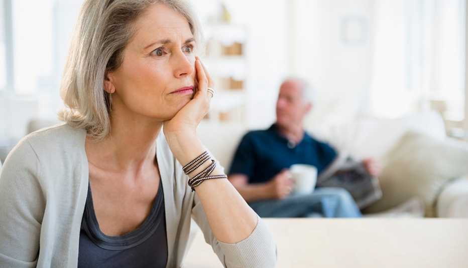 A female caregiver looking stressed as her husband relaxes on the couch behind her