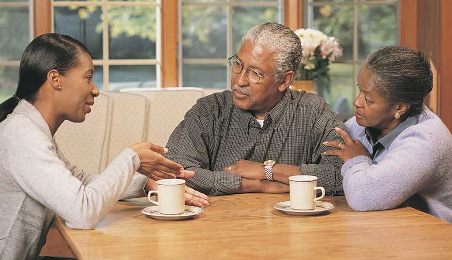 A woman speaks to her parents at a table in their home