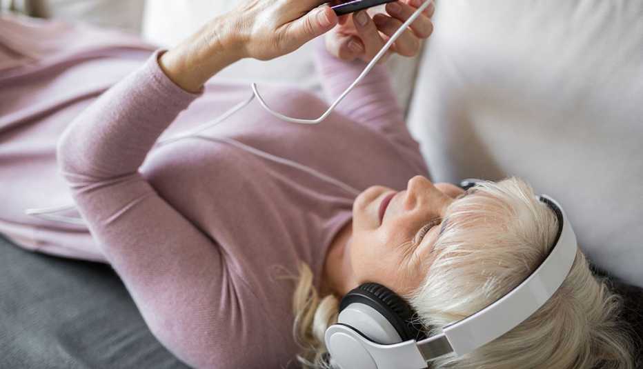 Glad senior lady lying on couch listening music on mobile