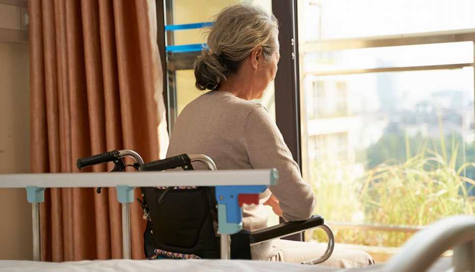 Rear view of a woman in a nursing home room sitting in wheel chair looking out the window