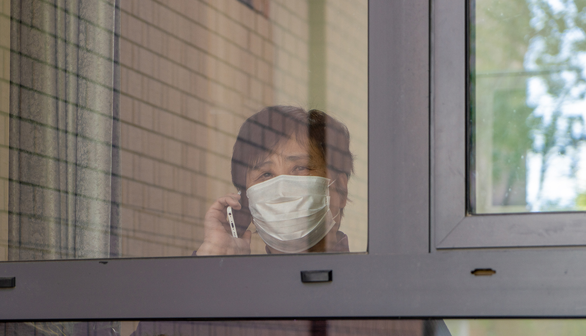 Woman wearing a face mask holding a telephone and looking out a nursing home window