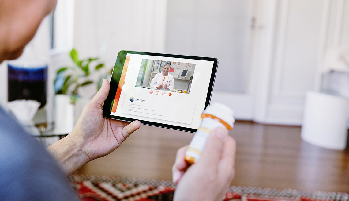 Male family caregiver holding a prescription bottle and video chatting with a doctor on a tablet during a telehealth call