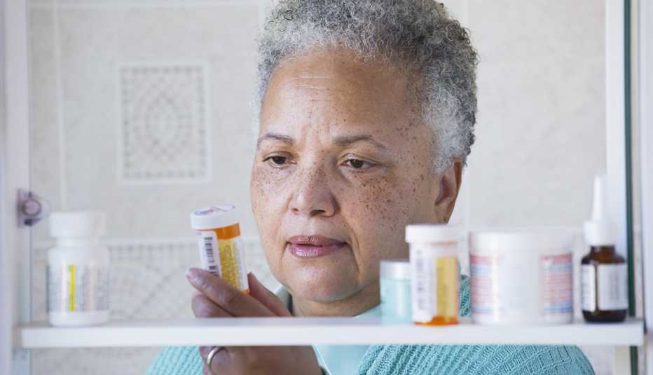 A woman standing in front of a medicine cabinet full of medication and holding a prescription pill bottle