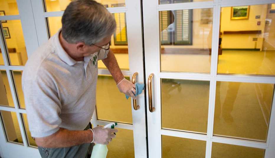 Man wearing gloves using disinfecting spray to clean a door handle at a nursing home