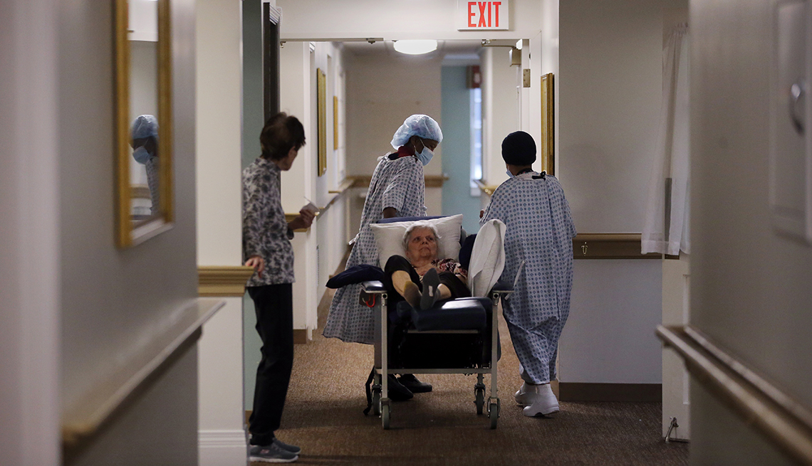 A nursing home resident being wheeled down the hall in a bed by workers wearing p p e 
