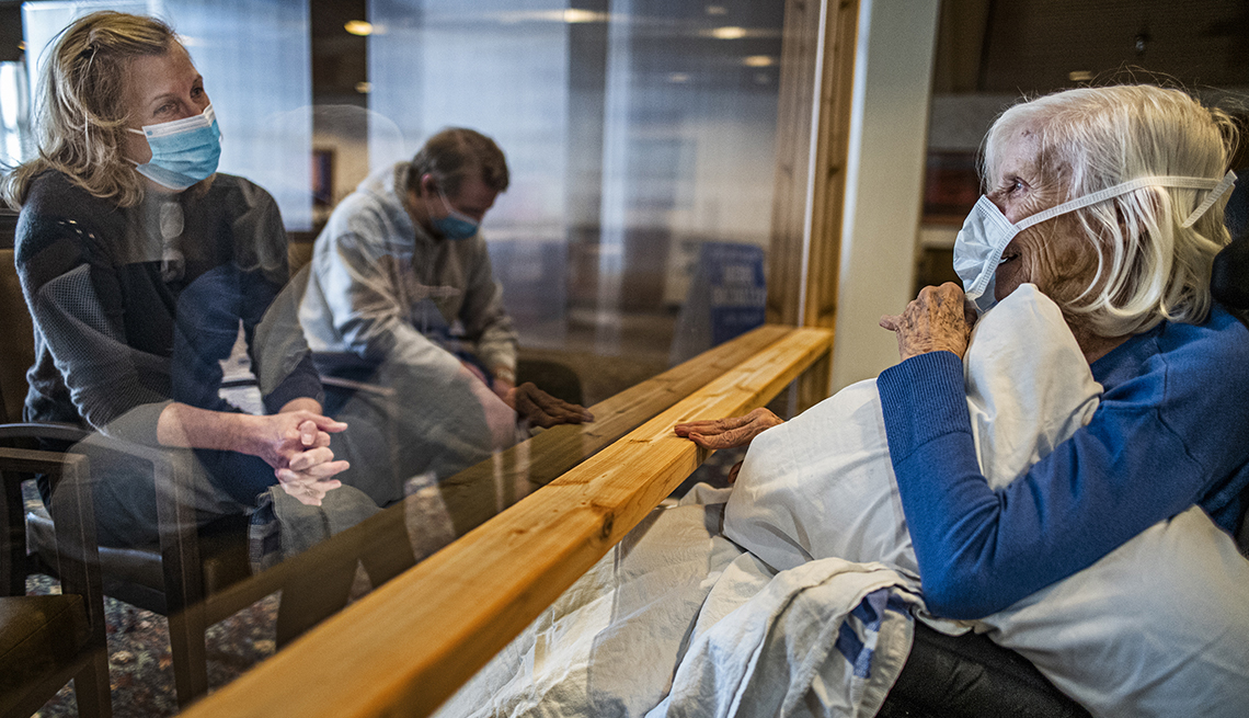 A female nursing home resident visits with her daughter and grandson through a glass partition