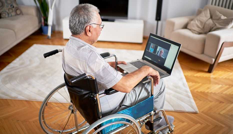 Man in his living room sitting in a wheelchair using laptop for a telehealth appointment with his doctor