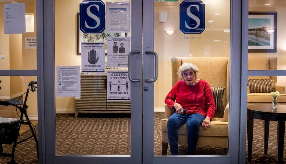 Woman sitting behind class doors of a nursing home with covid warning signs posted