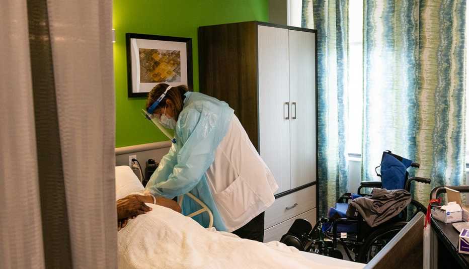  A nursing home worker wearing p p e checks on a resident laying in bed