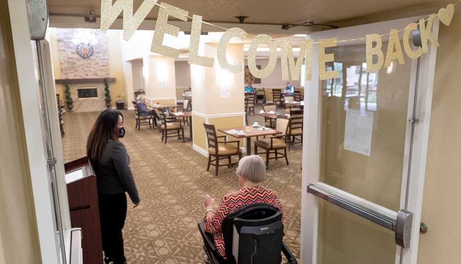 A nursing home resident in a wheel chair entering the home dining room under a sign that says welcome back