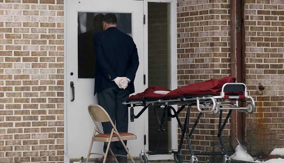 a funeral director standing next to an empty stretcher waits outside a nursing home door