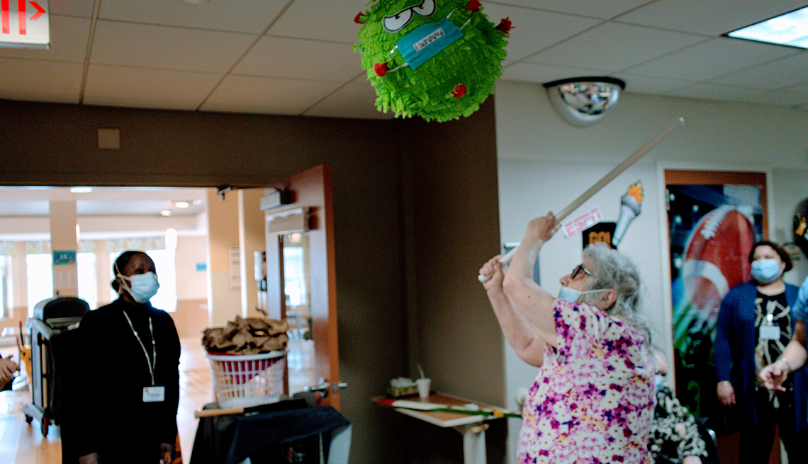 A female nursing home resident swinging a stick at a virus bug shaped piñata