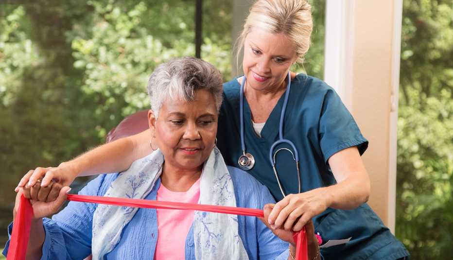 An older woman stretches an exercise band with the help of a female healthcare worker.