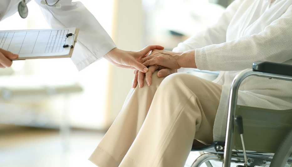 a doctor puts their hand over the hands of a patient in a wheelchair