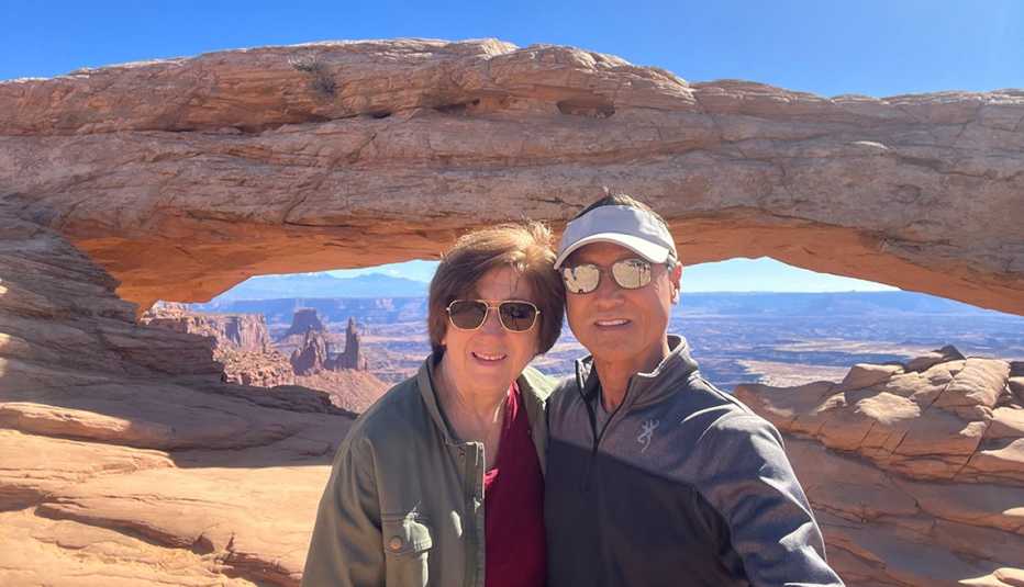 gina and gil kim posing on front of a natural rock bridge arch in utah on a recent trip