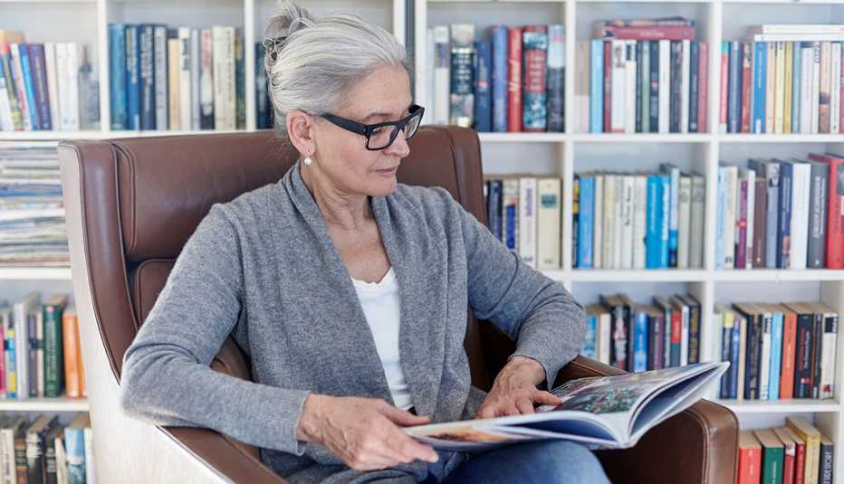 An older woman reads in an armchair, in front of a bookshelf.