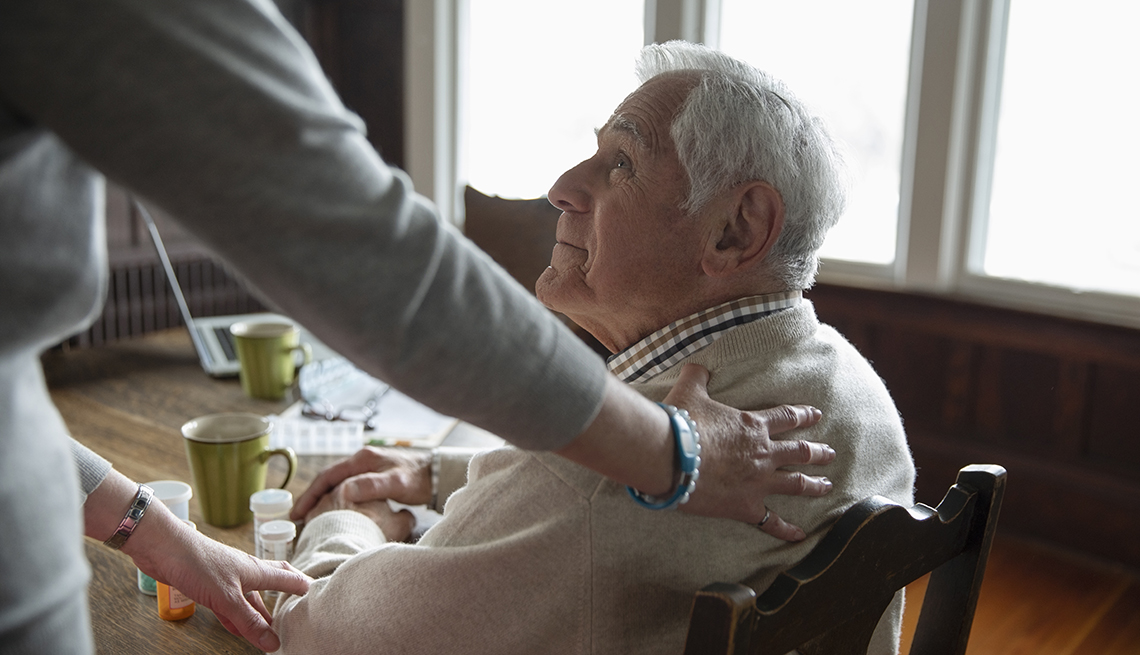 Home caregiver comforting senior man sitting at kitchen table